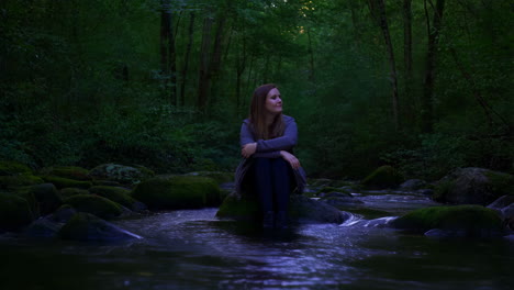 woman sitting on a rock in a forest stream