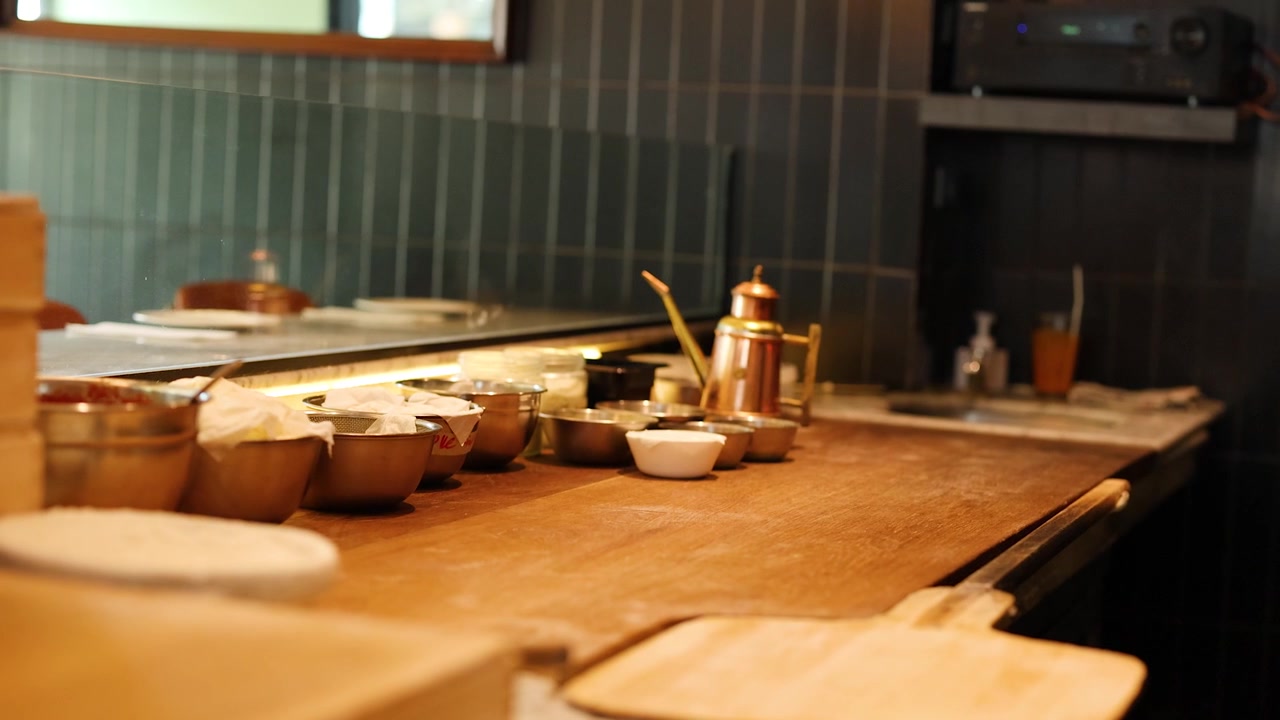 Static wide shot of an empty Italian kitchen counter with metal bowls and oil pot.