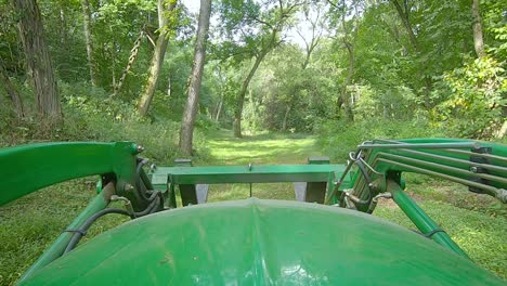 pov over the hood a loader with forks driving down a grassy path in the woods