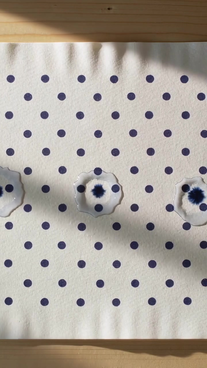 Vertical video: Moving shadow sliding over dotted sheet on wood table, three wet droplets spreading