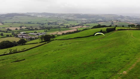 Shot-of-a-Paraglider-flying-along-a-ridge-of-a-hill-with-a-a-lovely-view-of-the-countryside-behind