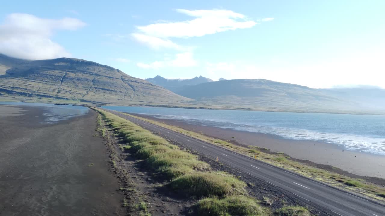 Explore the majestic coastal road and surf-laden shores near Vík í Mýrdal in South Iceland. Aerial footage captures misty mountain ridges under vivid skies, emphasizing the serene landscape