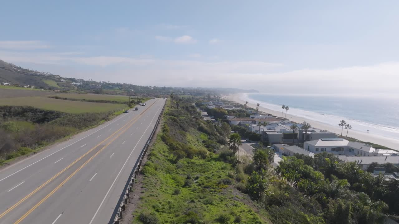 An aerial reveal shot showcases the Malibu, California sign as Highway 1 and the stunning coastline come into view, capturing the scenic meeting of road and ocean