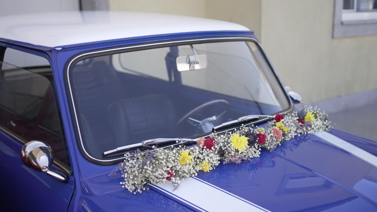 Vintage blue Mini Cooper adorned with colorful wedding flowers on the windshield