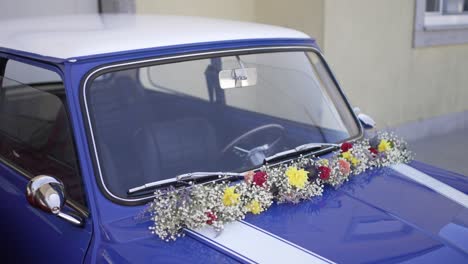 vintage blue mini cooper adorned with colorful wedding flowers on the windshield