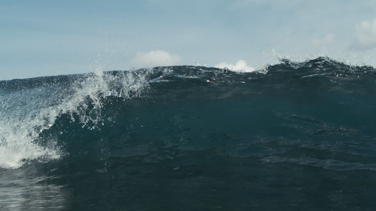Wave breaking in the distance with cloudy sky and subtle ocean texture, water glistens as lip throws forward