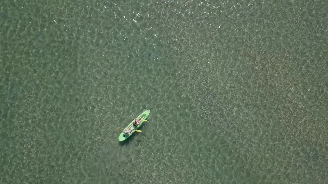 dos personas en remo de kayak sentado en la parte superior en aguas verdes poco profundas, aéreo