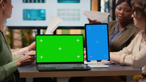 businesswomen working side by side with a green screen on the table