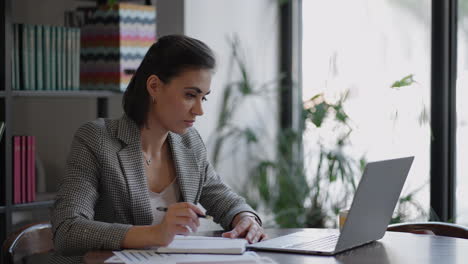 Business-woman-writing-something-in-notebook.-Start-up-woman-entrepreneur-student-studying-writing-note-at-workplace-near-computer.-A-womans-hand-writing-down-on-a-white-blank-notebook-on-table.