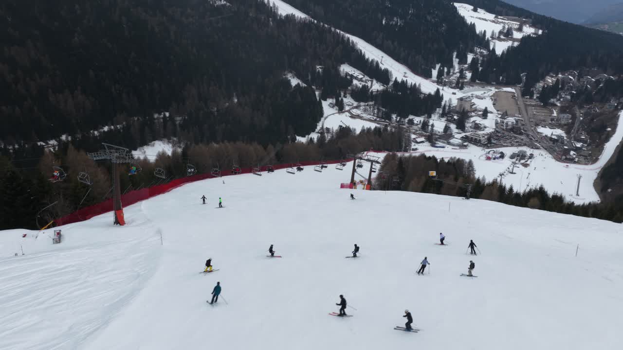 Filmato aereo con drone che mostra una rotazione fluida sopra una pista da sci a Folgaria, Italia, con sciatori in movimento e una seggiovia che attraversa la scena