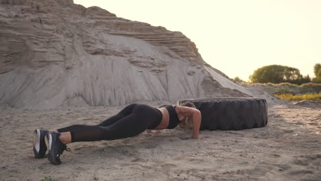 girl on sand quarry jumping burpee with push-ups through the wheel in the sand