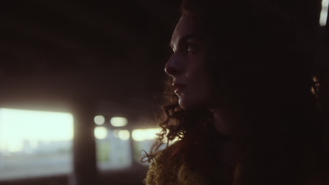 Woman with curly hair illuminated by red light in a dark urban setting