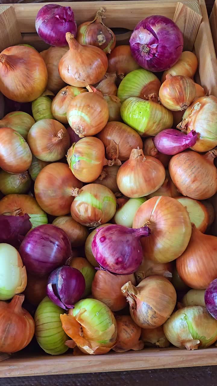 Static top-down shot of red and yellow onions piled together in a wooden crate, showing their natural texture and colors