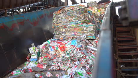 cinematic shot of bales of flattened milk and juice cartons on a conveyor in a recycling plant sill in bails of recycled material