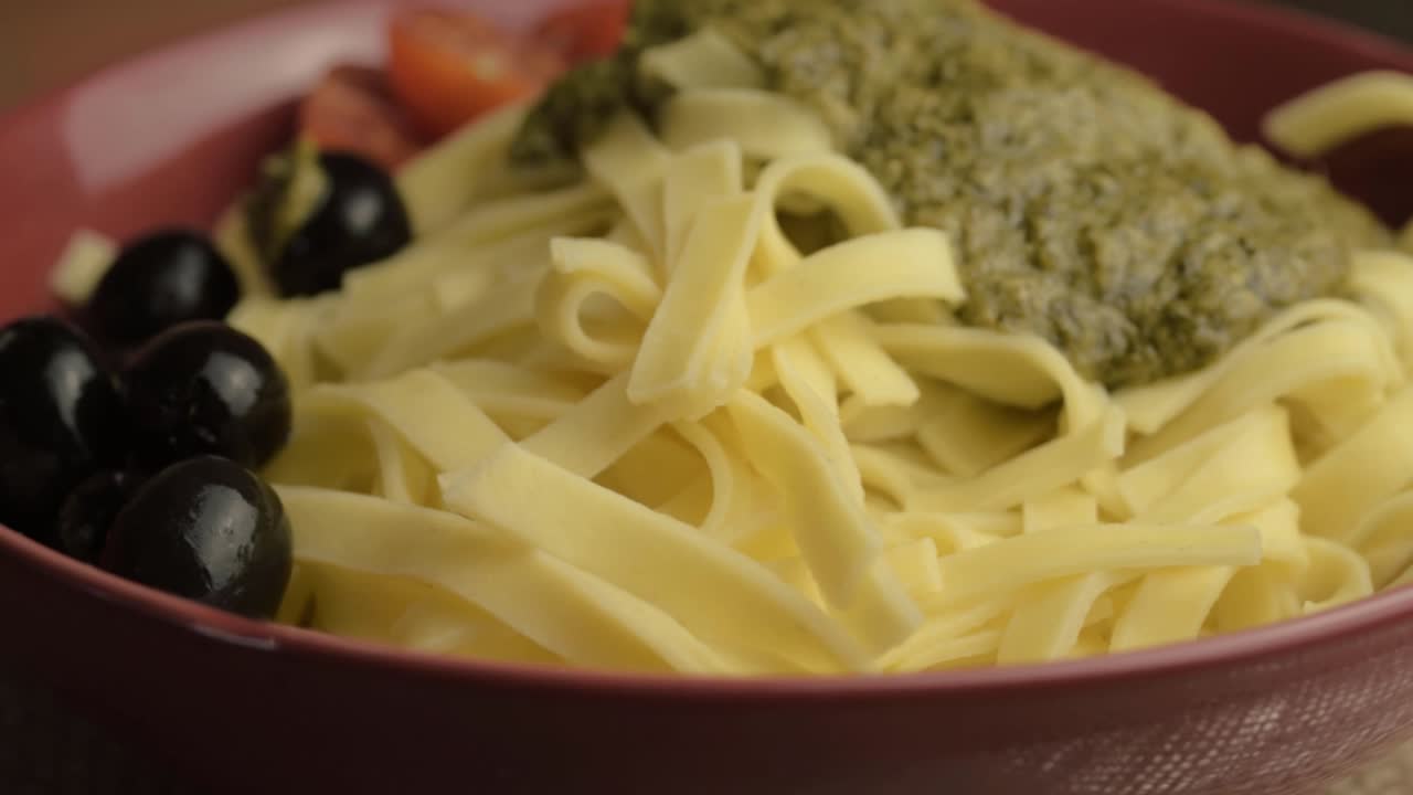 porción de pesto verde y pasta de tagliatelle con aceitunas negras en rotación de tiro medio