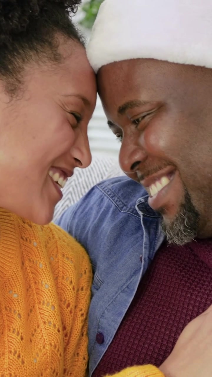 Vertical video: Leaning woman from left pressing foreheads on couch, man in denim shirt grinning