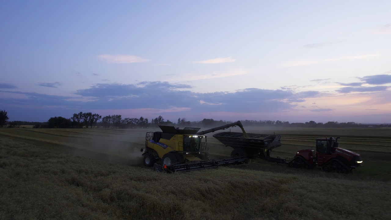 Combine Harvester Unloading Harvested Crops Into The Grain Cart In Twilight. - aerial pullback shot