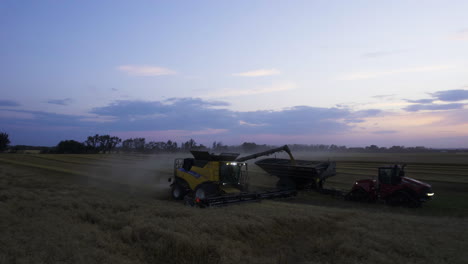 combine harvester unloading harvested crops into the grain cart in twilight. - aerial pullback shot