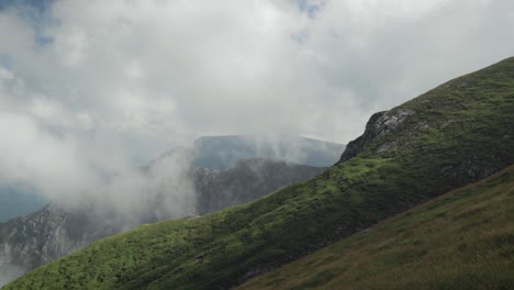 Schwenk-Von-Links-Nach-Rechts-Auf-Einen-Steilen-Berg-Mit-Niedrigen-Wolken-Und-Berggipfeln-Im-Hintergrund