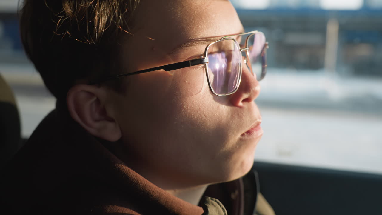 close up of red car window reflecting office building and student eating chocolate and sipping juice inside parked car with blurred winter urban backdrop conveying candid snack moment