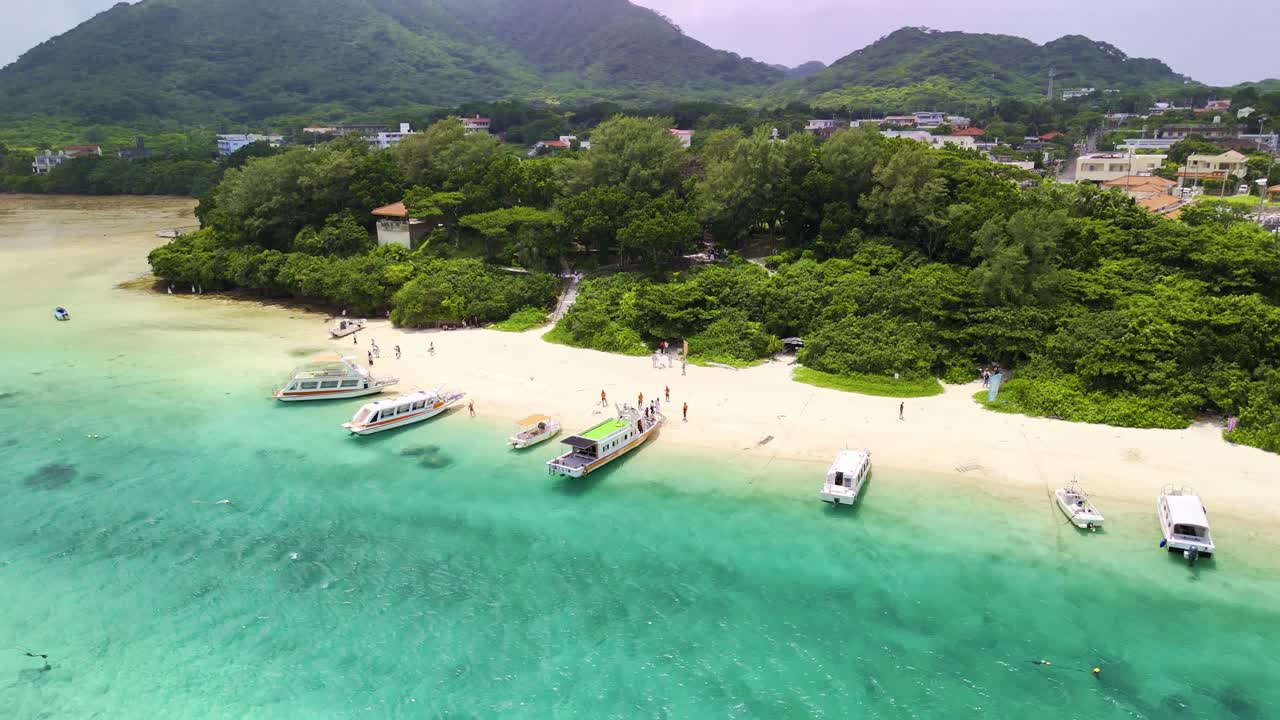 Ripresa con drone di turisti che si imbarcano su barche turistiche sulle bianche spiagge sabbiose di Kabira Bay, Ishigaki, circondati da acque turchesi e una lussureggiante vegetazione tropicale.