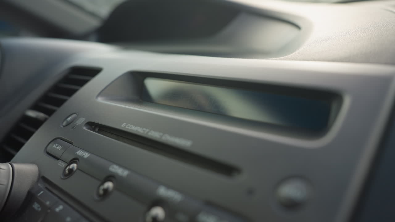 close up of dashboard showing stereo control panel and cd display screen blinking inside parked car under daylight with visible air vent and buttons around media console