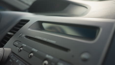 close up of dashboard showing stereo control panel and cd display screen blinking inside parked car under daylight with visible air vent and buttons around media console