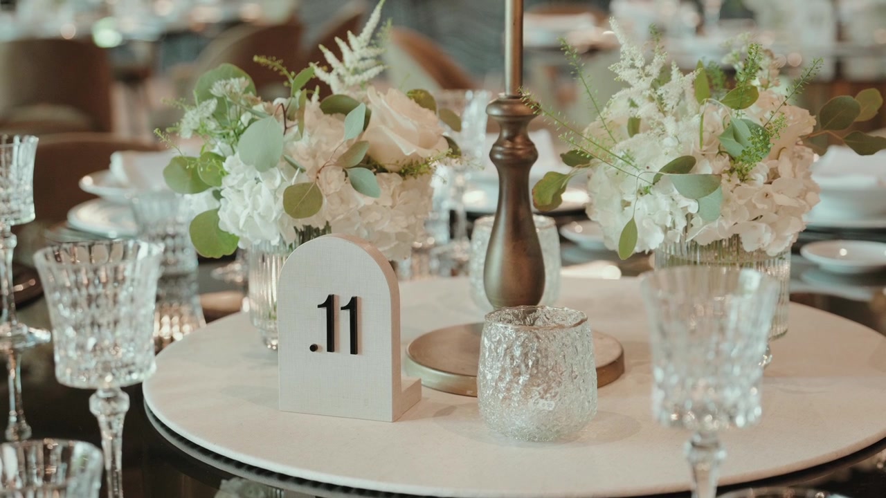 Table number sign beside white flowers crystal glasses and gold candlestick on a set table