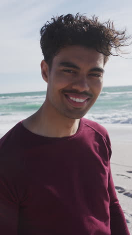 video vertical del retrato de un hombre biracial feliz en una playa soleada