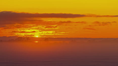 Amanecer-Dorado-épico-Con-Destello-De-Lente-De-Nubes-Voladoras-Y-Niebla-En-El-Campo-De-Invierno-Cubierto-De-Nieve---Lapso-De-Tiempo