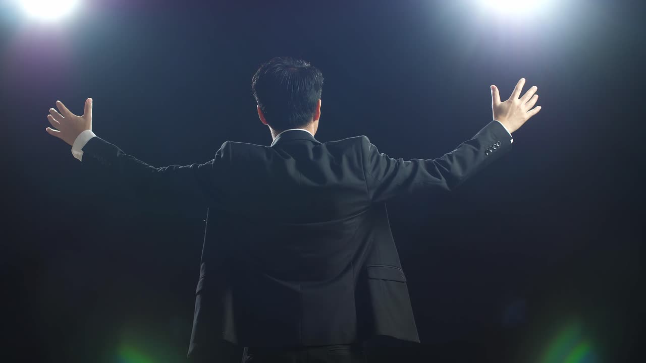 블랙 스크린 스튜디오에서 팔을 펴고 있는 비즈니스 슈트를 입은 아시아 스피커의 뒷면