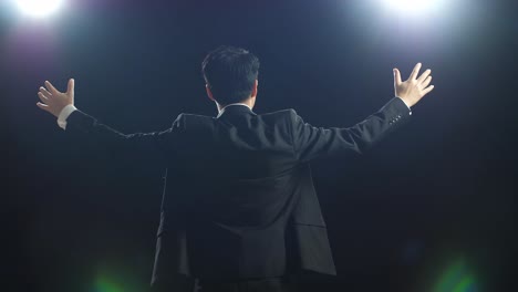 back view of asian speaker man in business suit spreading out his arms in the black screen studio