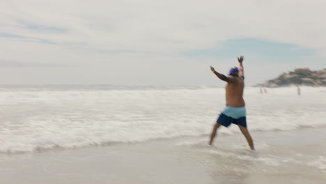 Lustiger-Afroamerikanischer-Mann,-Der-Mit-Flossen-Am-Strand-Im-Meerwasser-Spaziert-Und-Sich-Zum-Schwimmen-Bereit-Macht,-Um-Den-Sommer-Am-Meer-Zu-Genießen,-4k