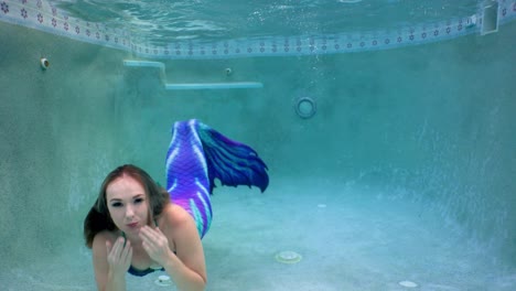 bajo el agua nadar en una piscina con una sirena mientras ella sopla besos y burbujas de aire