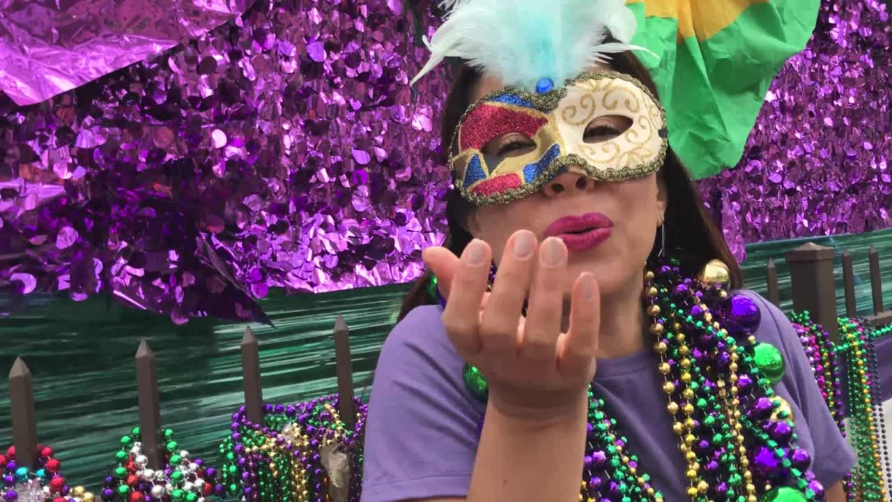 una joven turista latina, con máscara, trajes y collares celebrando el mardi gras por las calles de nueva orleans.
