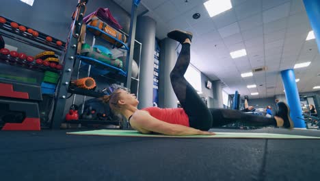 Young woman doing workout in gym. Sportive girl lying on a mat and lifting her legs together on the background of fitness center.