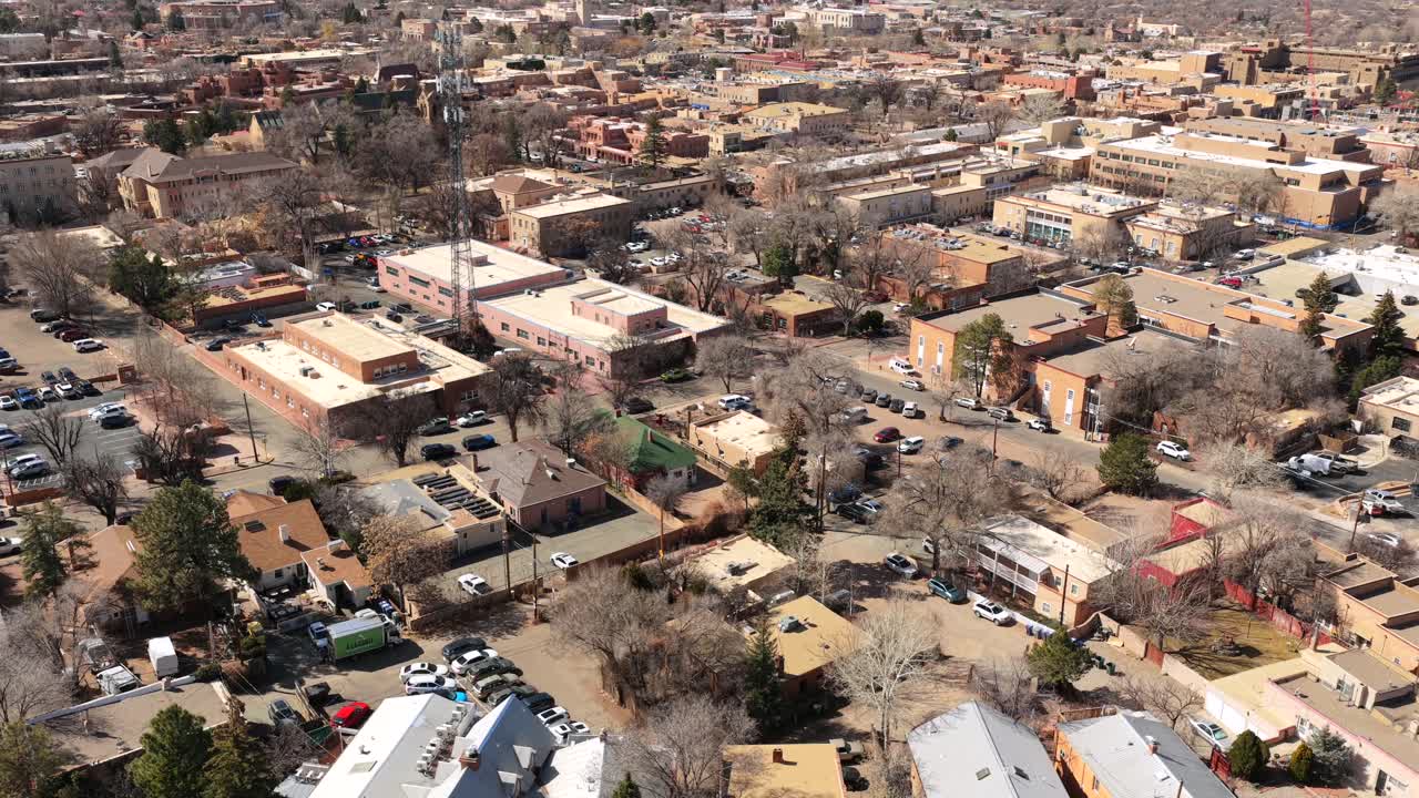 A high-altitude drone perspective overlooks the iconic adobe rooftops and urban sprawl of Santa Fe. This 4K view captures the city's unique architectural harmony and mountain horizon