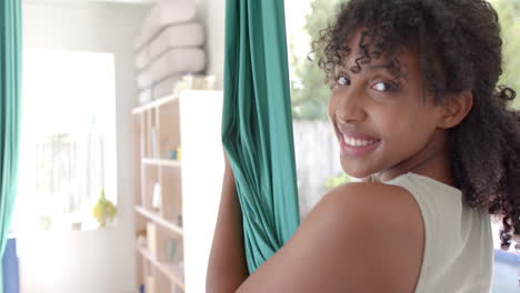 Portrait-of-happy-biracial-teenage-girl-exercising-in-aerial-yoga-class,-slow-motion