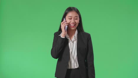 A Smiling Asian Business Woman Talking On Mobile Phone While Walking In Front Of Green Screen In The Studio