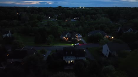 turning car on street of luxury american neighborhood at dusk. housing area with single family houses at night. lighting buildings and homes in suburbia. aerial approaching shot.