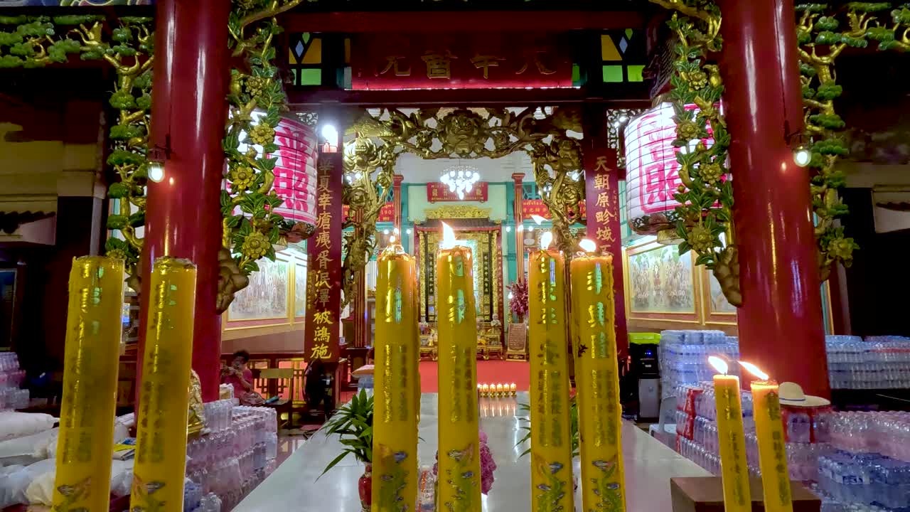 Tall yellow candles burn on ornate altar, vibrant temple interior, low light, slight camera movement