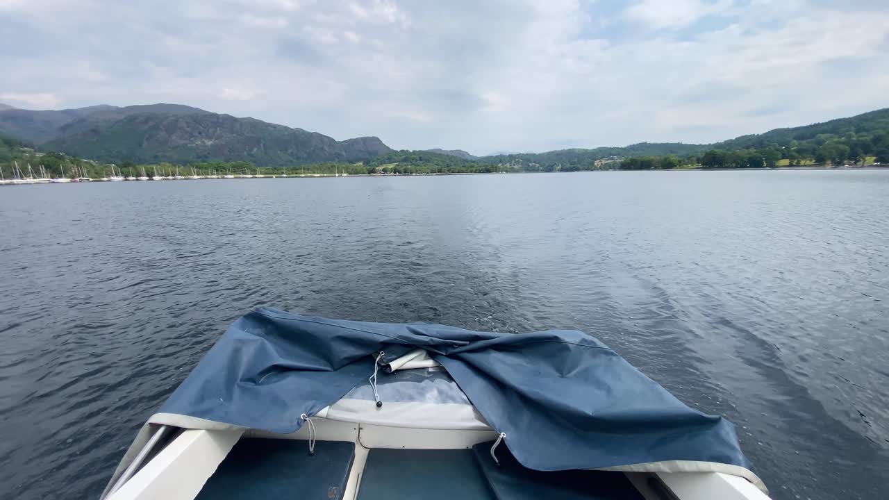 mirando por la parte trasera de un pequeño bote de motor blanco a una vista montañosa, rodeando el agua de coniston en el distrito de los lagos, reino unido