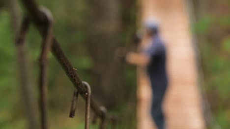 man walking on a wooden suspension bridge in the forest