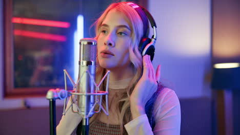 Woman singing into a microphone with headphones in a studio