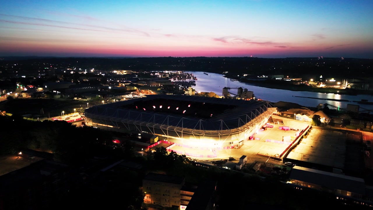 Elevated drone view of glowing St Marys Stadium and River Itchen waterfront beneath a soft blue and magenta dawn sky