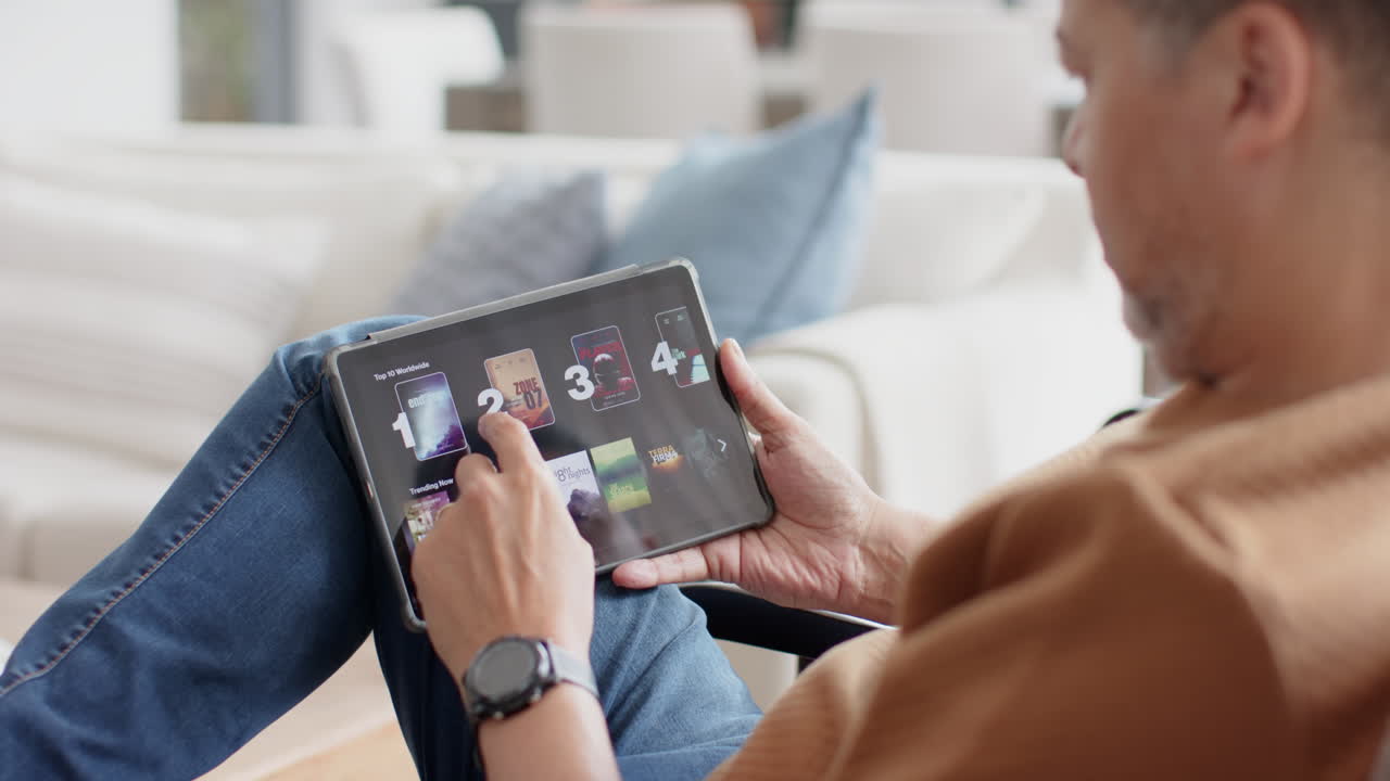 hombre biracial mayor usando tableta sentado en la sala de estar soleada en casa, cámara lenta