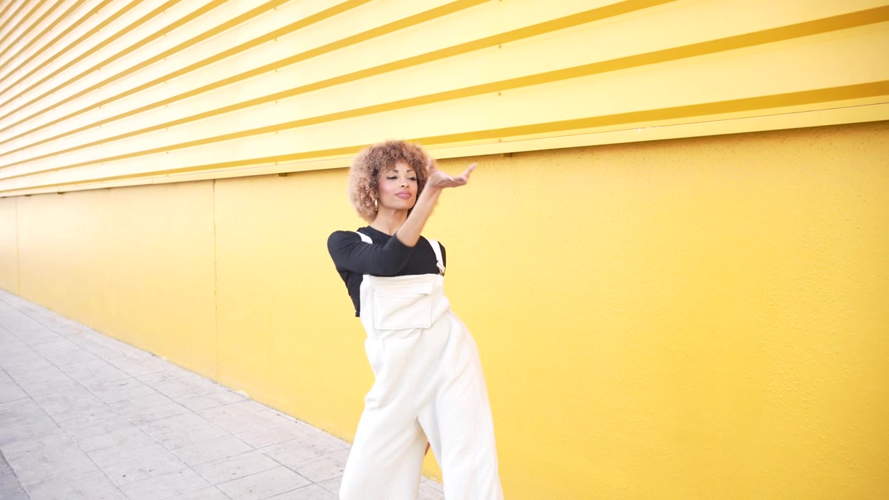 A stylish and young woman posing confidently against a bright yellow wall in an artistic setting