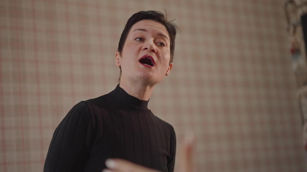 Experienced teacher demonstrating vocal technique closeup of instructor projecting tone and articulation against plaid backdrop, precise diction, controlled breath, classroom atmosphere, professional