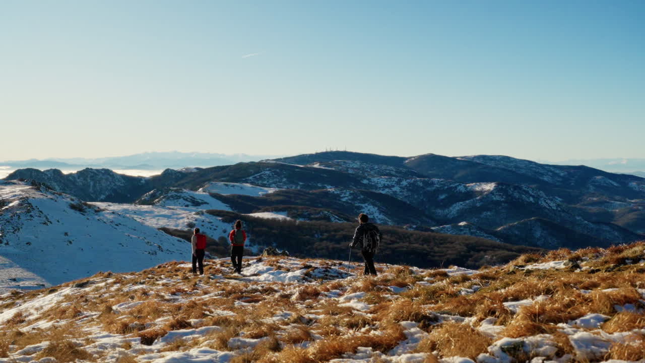 Campo lungo di tre escursionisti che camminano con i bastoncini su una cresta montuosa innevata