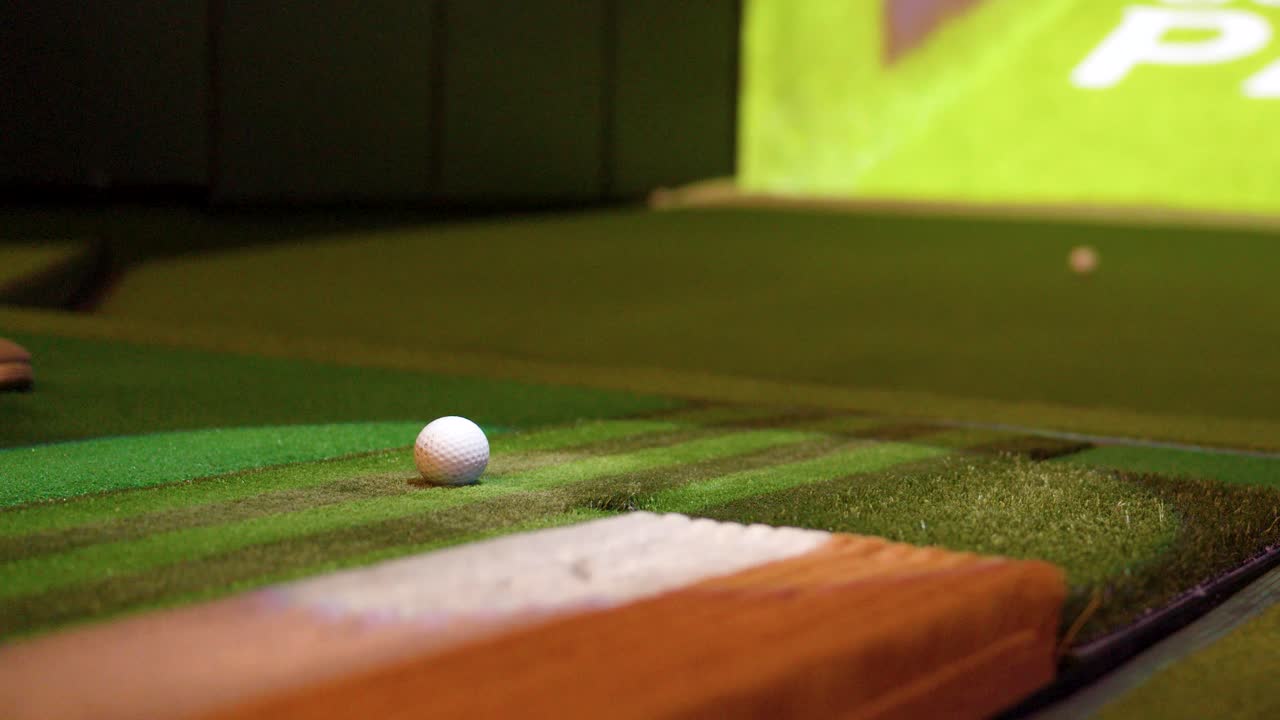 Un primo piano da angolazione bassa mostra una mazza da golf che colpisce una palla su erba sintetica.